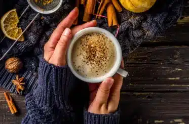 hands clasped around a pumpkin spice coffee cup with cinnamon and a gourd around