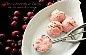 Cherry Amaretto Ice Cream from The Coconut Mama (dairy free) Cherry amaretto ice cream in a scoop with three more scoops of ice cream in a bowl