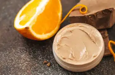 Orange chocolate body butter in a small container with an orange slice behind it