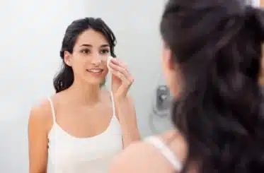 woman looking in a mirror and holding makeup remover pad to her face