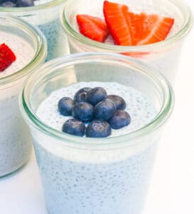 Chia seed pudding in three glasses; one is topped with blueberries, one topped with strawberries, and one topped with raspberries