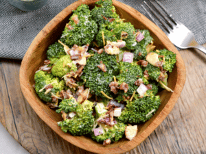 keto broccoli salad with red onions, bacon, and broccoli all visible in a brown bag with a fork behind