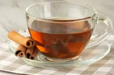 cinnamon tea in a glass mug with cinnamon sticks on a glass saucer with a checked cloth below