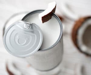 Picture of an opened can of coconut milk with a coconut slice placed on the rim.