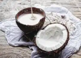 coconut milk pouring into a half coconut shell, with another half coconut with meat and liquid next to it