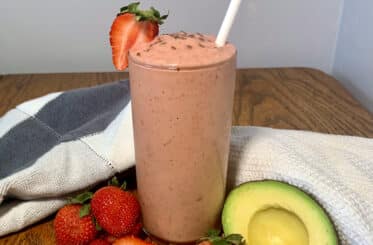 keto strawberry avocado smoothie on a table with ingredients nearby