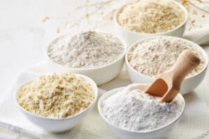 5 different bowls of variously-colored flour. A wooden ladle in one of them.