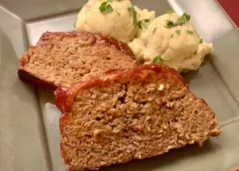 Two juicy slices of Easy Ketchup Meatloaf on a green plate with two mounds of homemade mashed potatoes.