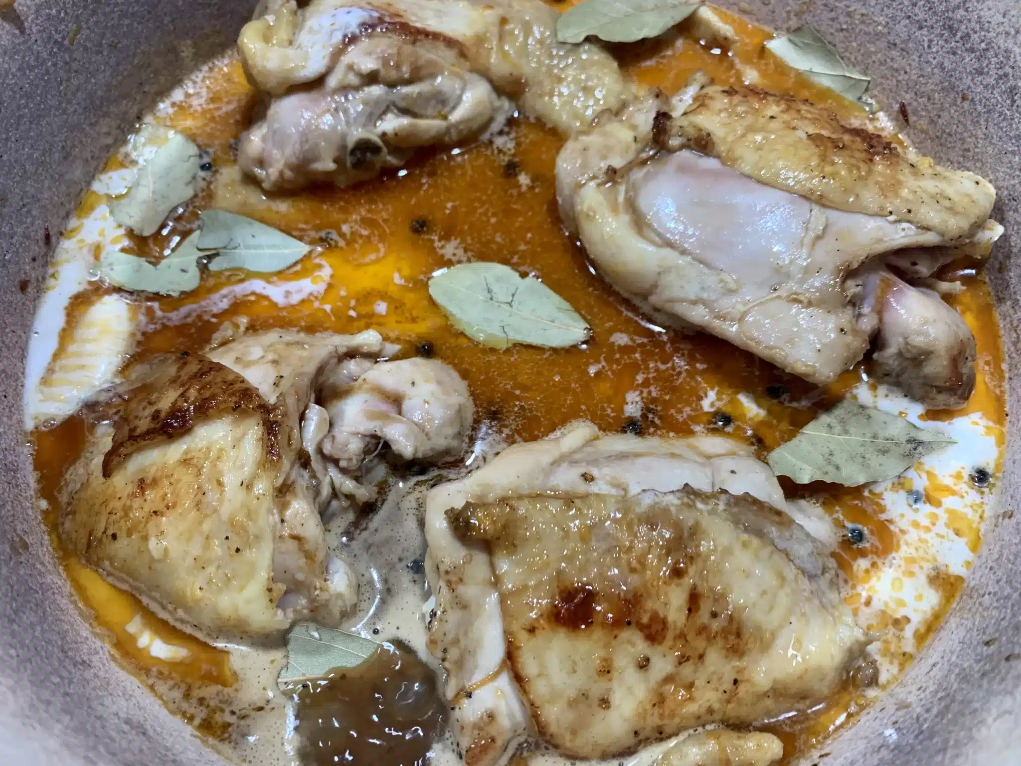 chicken cooking in a brown sauce with coconut milk and bay leaves