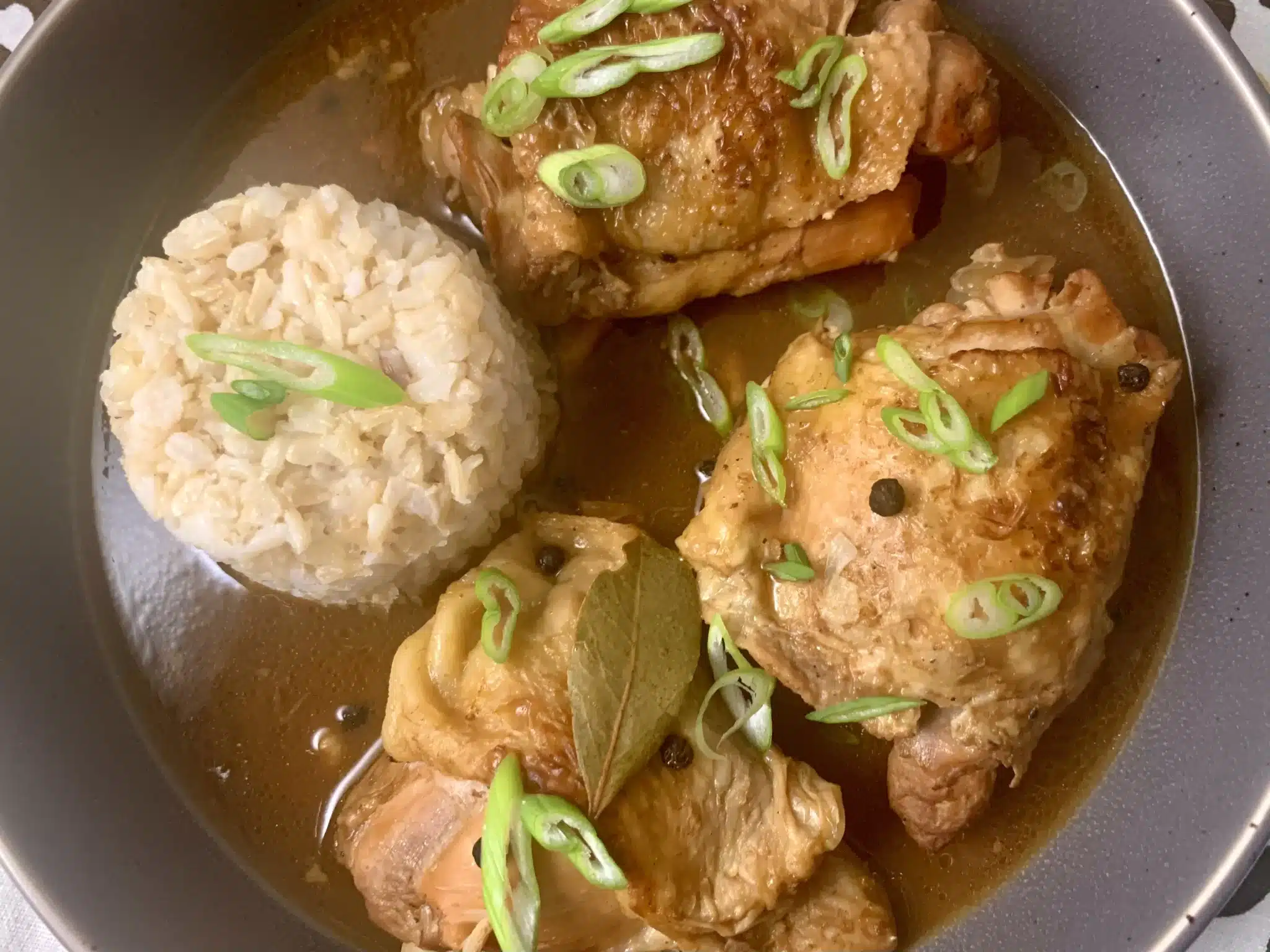 adobo chicken with green onions and bay leaves on top and rice next to them