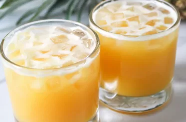 two cups of pineapple coconut juice with a pineapple posed behind