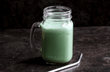 clear jar of matcha pineapple drink with a metal straw next to it
