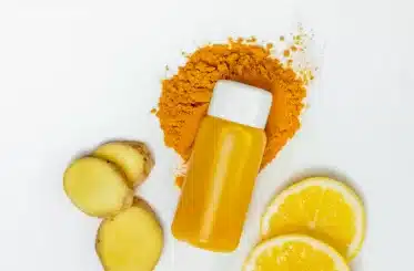 homemade ginger shot in a bottle with ginger powder right under it and slices of lemon and ginger scattered around, as seen from above
