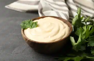 homemade coconut oil mayo in a brown bowl with a sprig of green in it and a striped cloth in the background