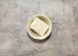 Top view of a piece of shortening in a bowl resting on a gray background.