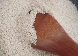 A pan full of sesame seeds with a wooden spatula stirring them.