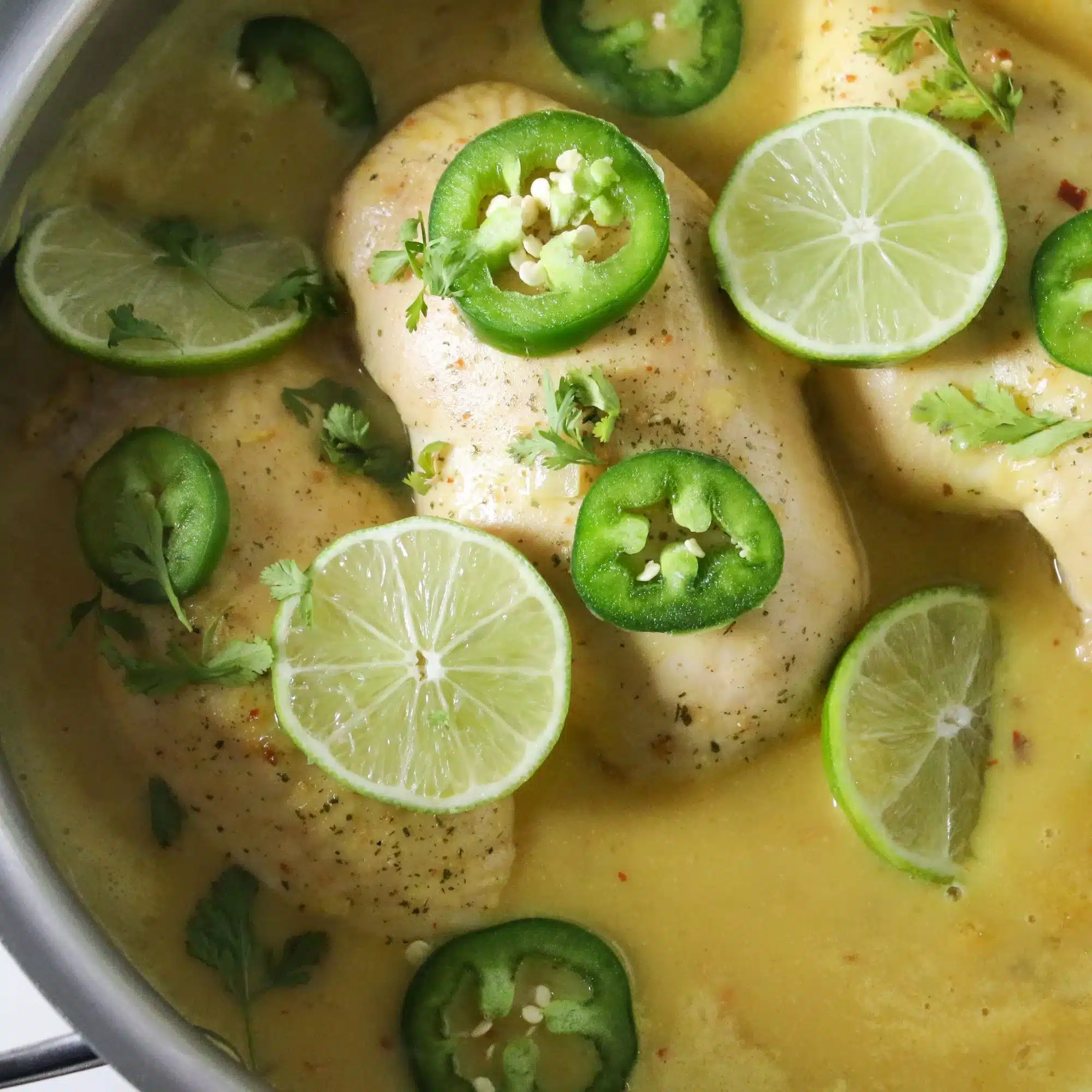 Cooked chicken breasts in a sauce and topped with lime wedges. 