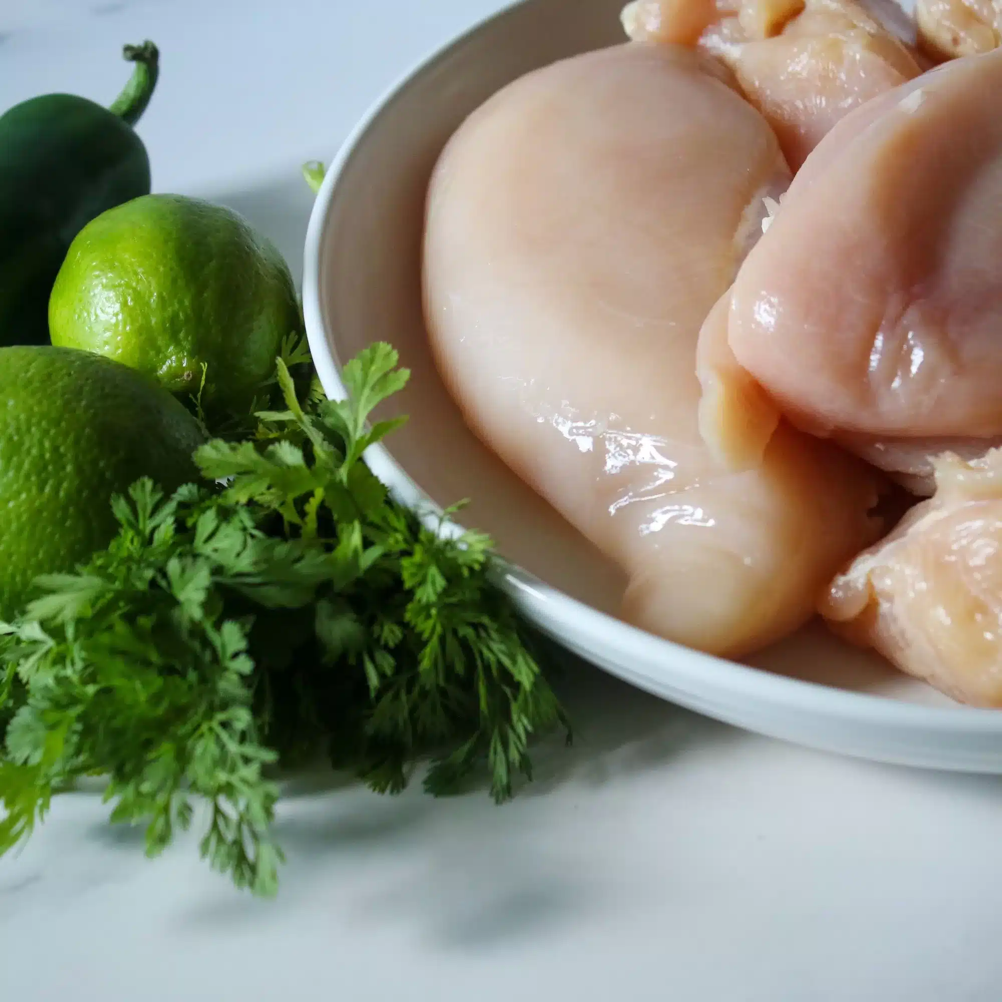Chicken breasts, lime, and cilantro all setting on a counter. 