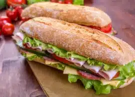 Sub sandwich with lettuce, tomato, ham, and cheese on a wooden table.