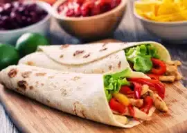 Two chicken fajitas with lettuce and red peppers on a wooden board.