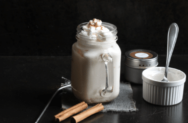 Starbucks Horchata Frappuccino in a glass mug with cinnamon sticks and containers around it, all on a black background
