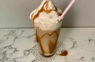 Copycat Starbucks caramel latte in a glass with a straw and caramel dripping over the side of the cup