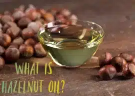 A bowl of hazelnut oil between two mounds of hazelnuts. The text reads, "What is hazelnut oil?"