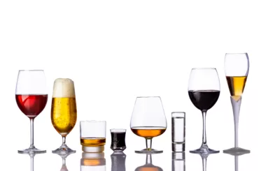Assorted alcoholic drinks in different glasses on white background.