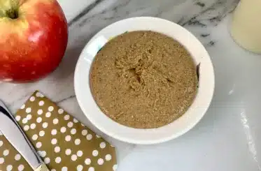 Soy Nut Butter in a white bowl on a marble countertop with a knife and a Honeycrisp apple