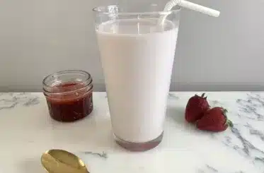 Strawberry milk on a marble countertop with strawberries and homemade strawberry syrup in a glass jar