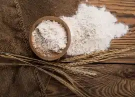 Aerial view of a clay containing durum flour next to a pile of the same flour set with a few wheat ears on a wooden bakground.