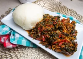 A plate containing Pounded Yam Fufu and Efo Riro resting on a pair of different checkered napkins.