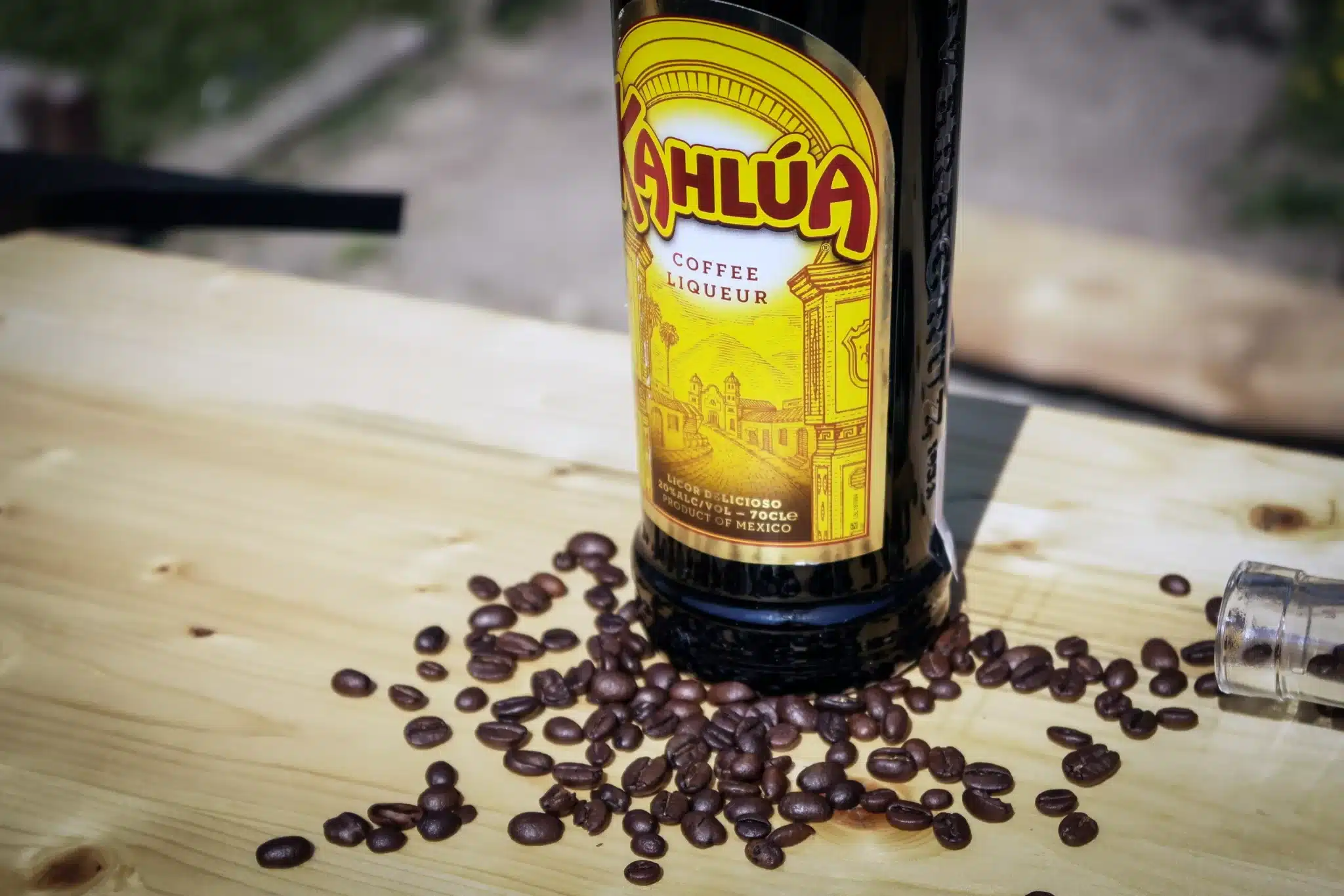 A wooden table showcasing a bottle of Kahlua surrounded by coffee beans.
