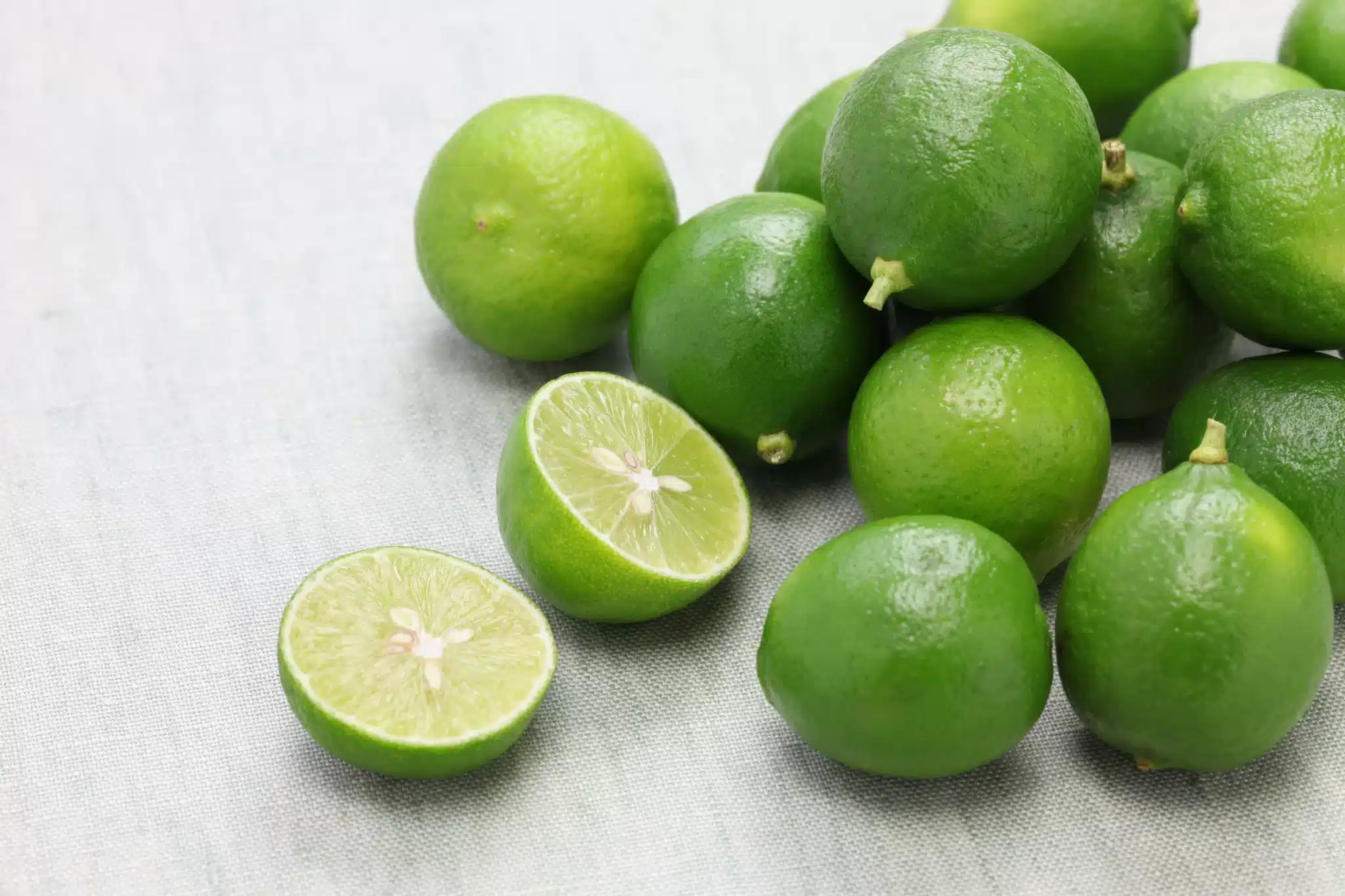 Some entire key limes and a halved one scattered over a tablecloth.