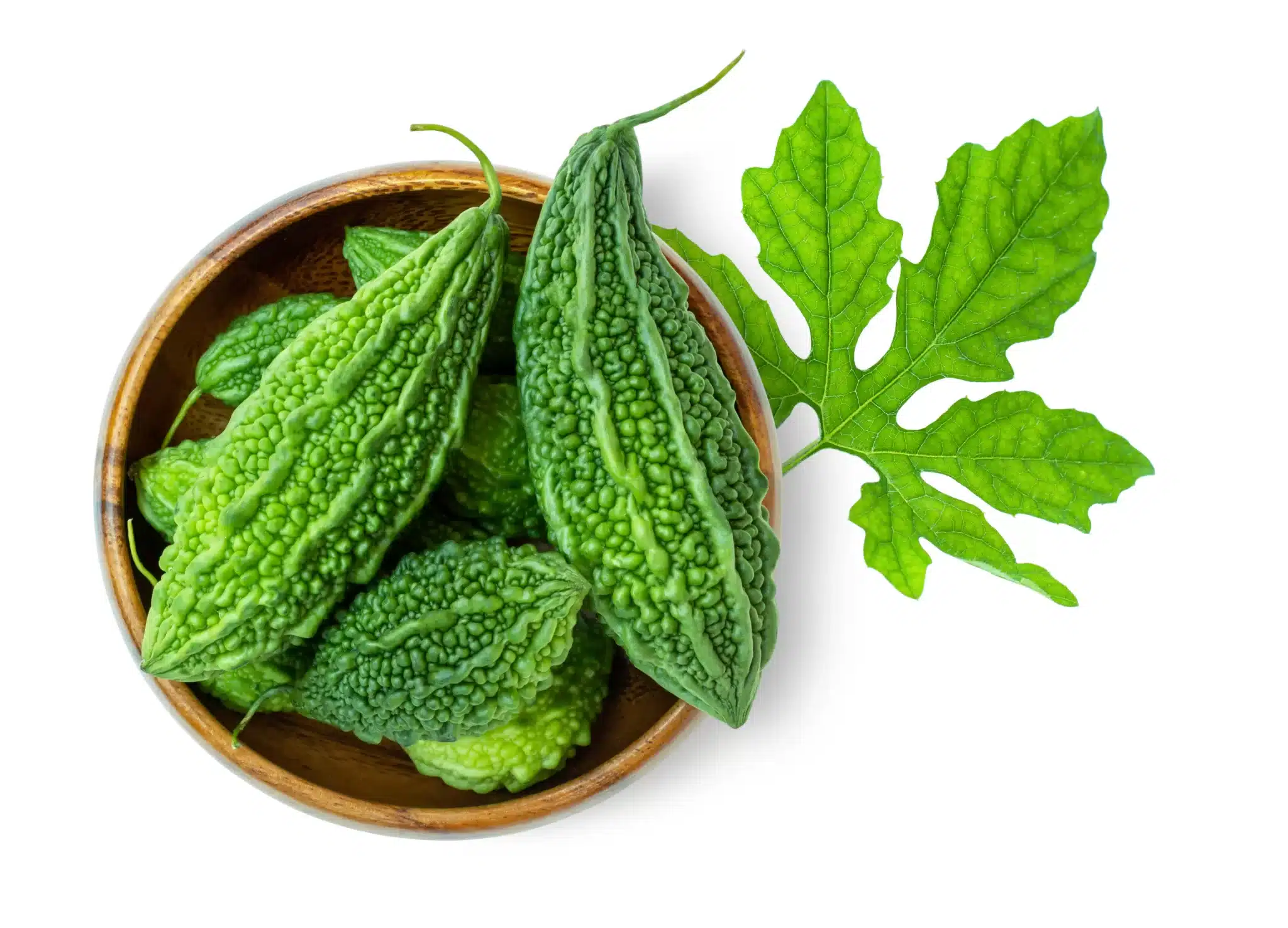 Overhead shot of a bowl containing karelas next to a leaf.