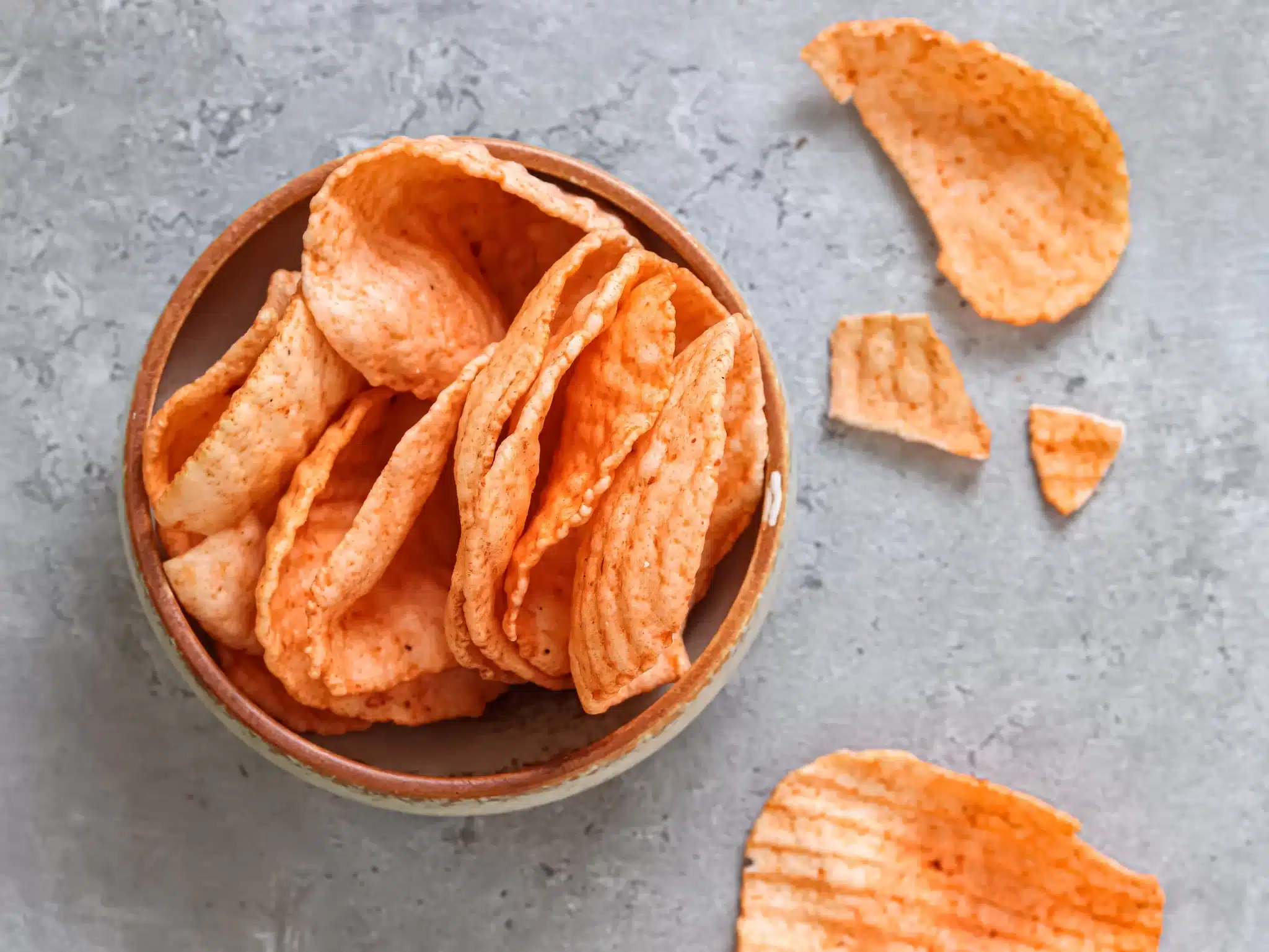 A bowl heaped with keripik kentang with some of them scattered nearby.