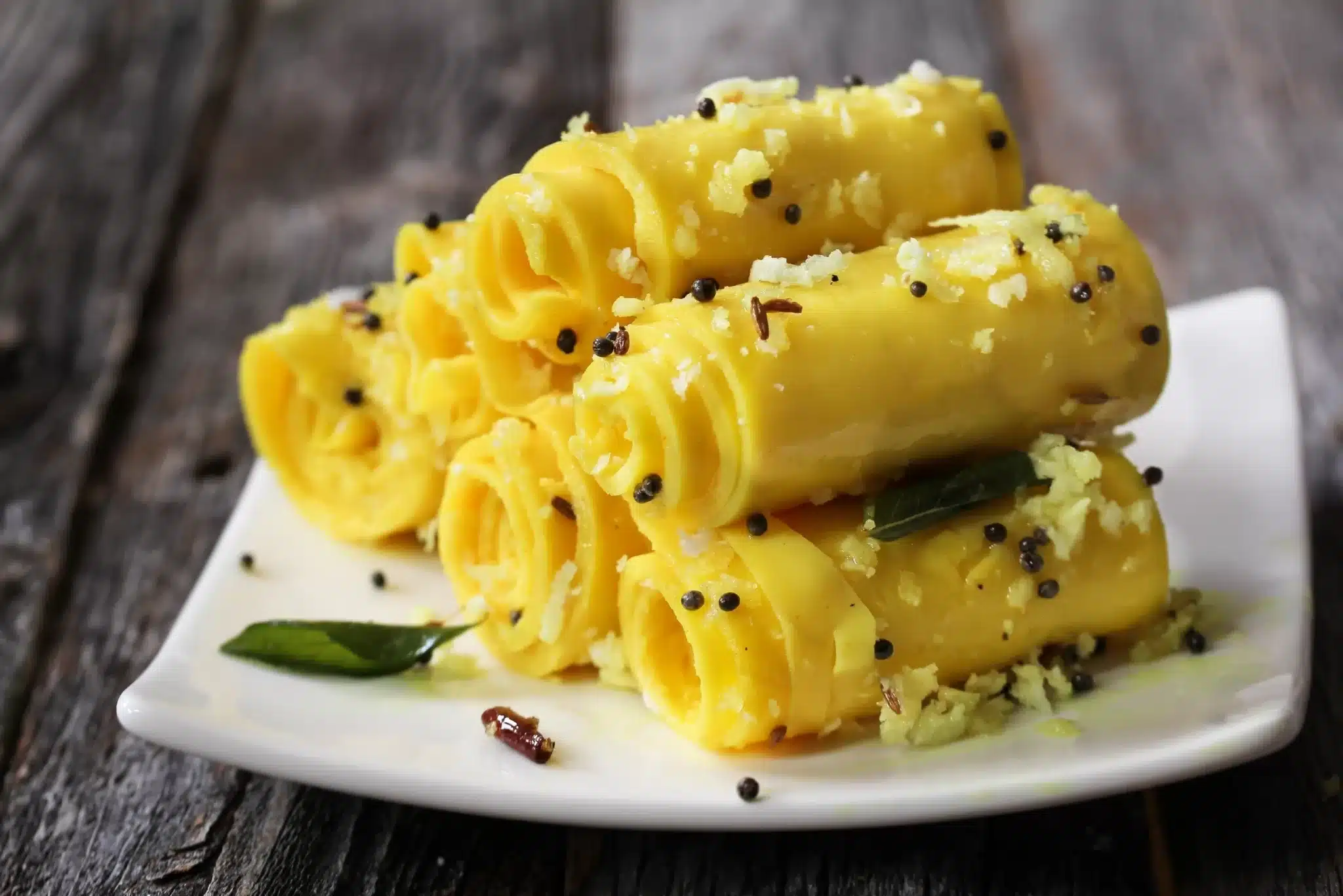 A plate holding a pile of khandvi pieces. 