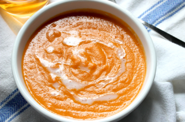 Apple Cider Vinegar Carrot and Ginger Soup in a white bowl over a white and blue striped napkin