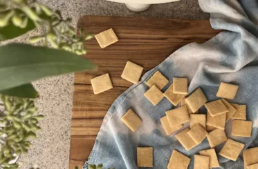 Homemade almond flour crackers scattered across a blue kitchen towel surrounded by greenery and a bowl of apples.