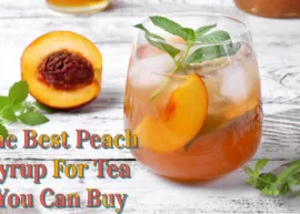 A rustic table displaying a glass of iced tea prepared with peach syrup and a few peaches. The text reads, "The Best Peach Syrup For Tea You Can Buy."