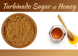 Overhead view of a bowl containing turbinado sugar, a jar of honey, and a wooden honey stirrer.