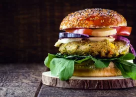 Close-up of a vegetarian burger with leafy greens, patty, cheese, onion, tomato, and seeded bun.