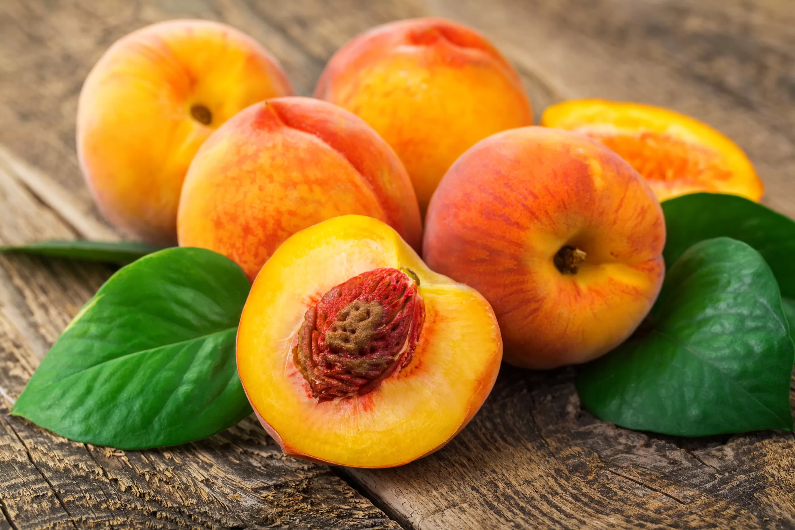A wooden table showing a few last chance peaches and leaves. 