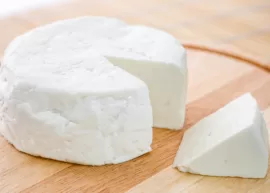 A round white cheese wheel with a wedge cut out on a wooden board.