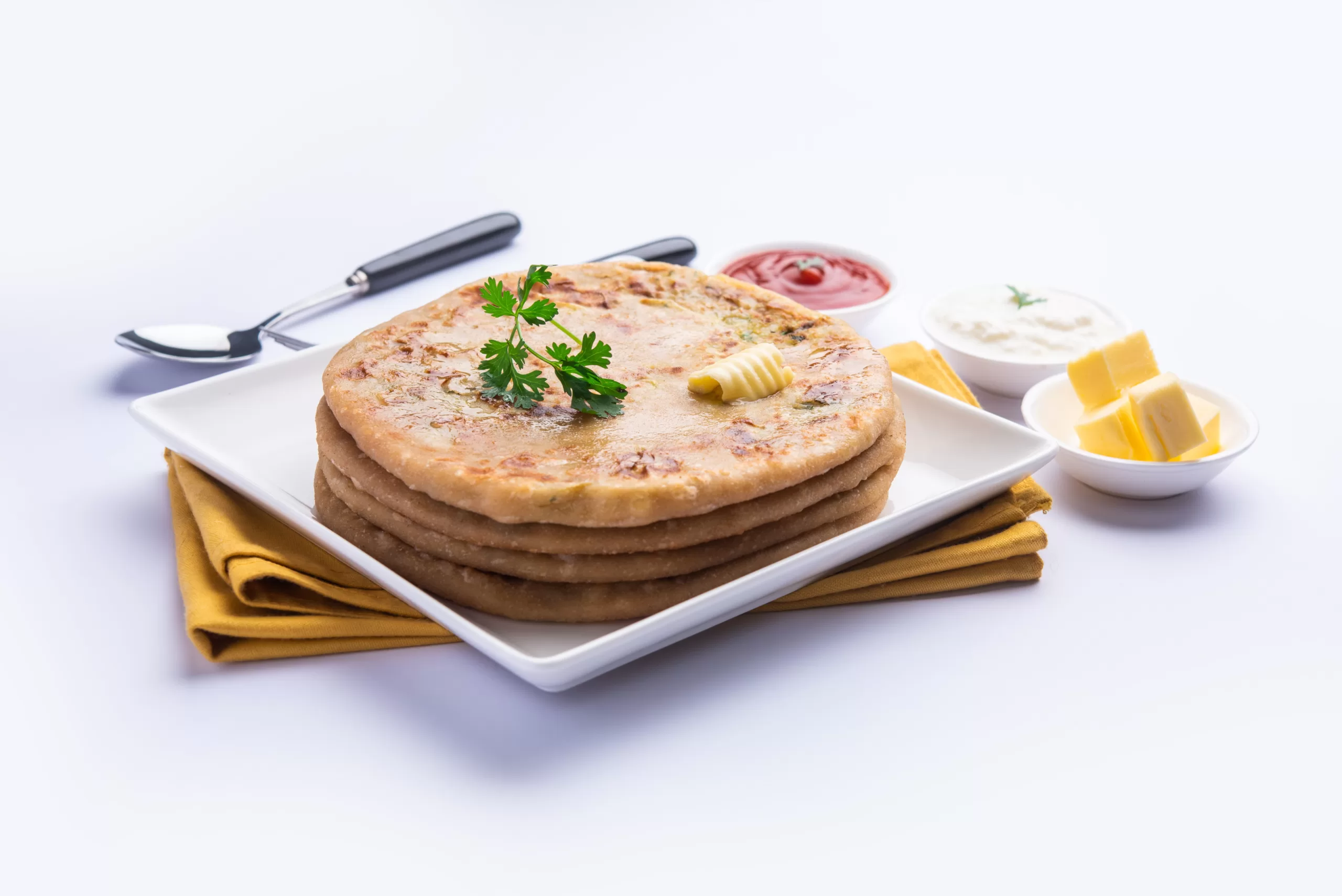 A ceramic plate with a stack of paratha pieces, accompanied by butter and a couple of dips.