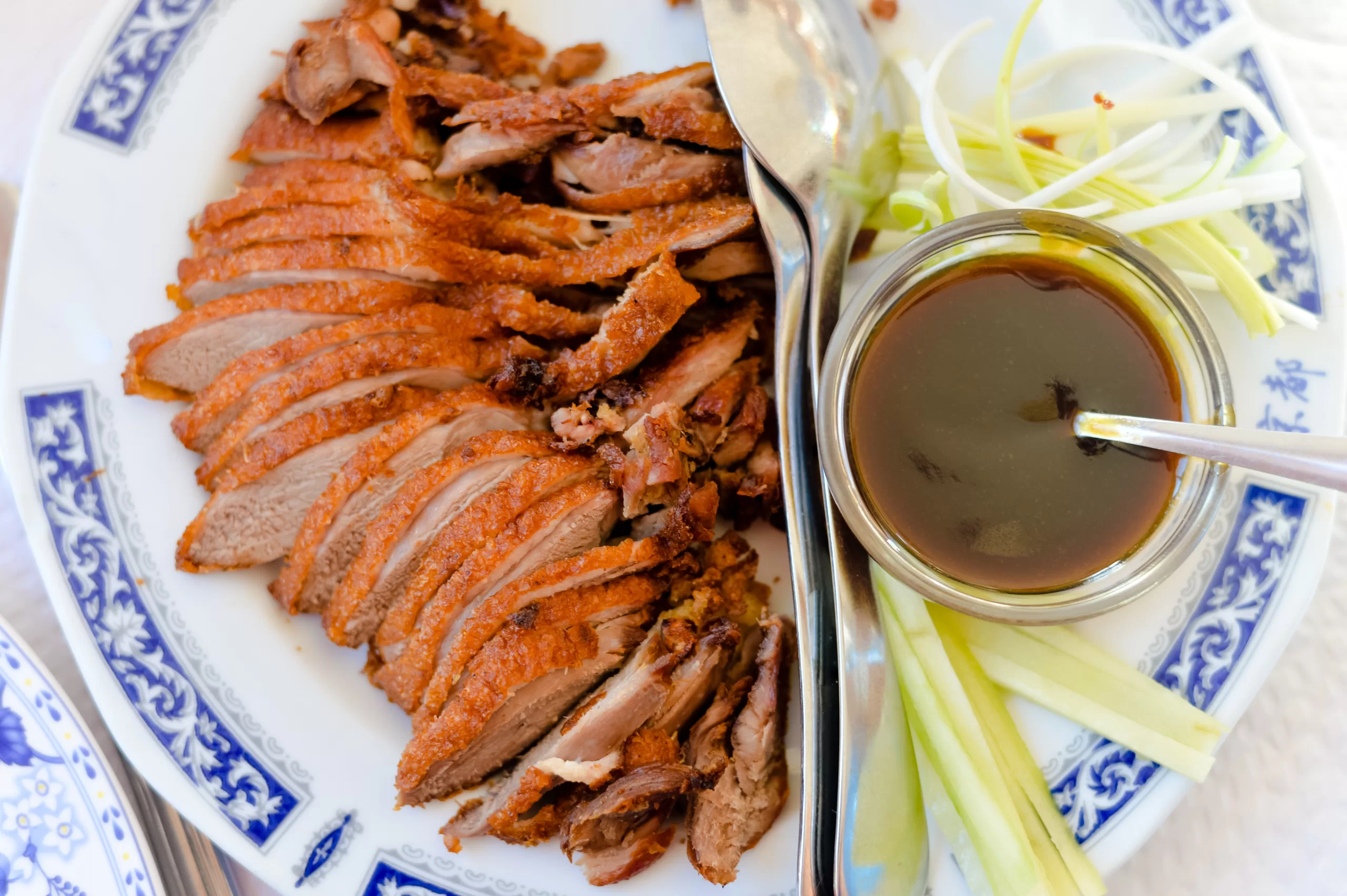Aerial view of a Peking duck cut in slices, a sauce, and some vegetables. 