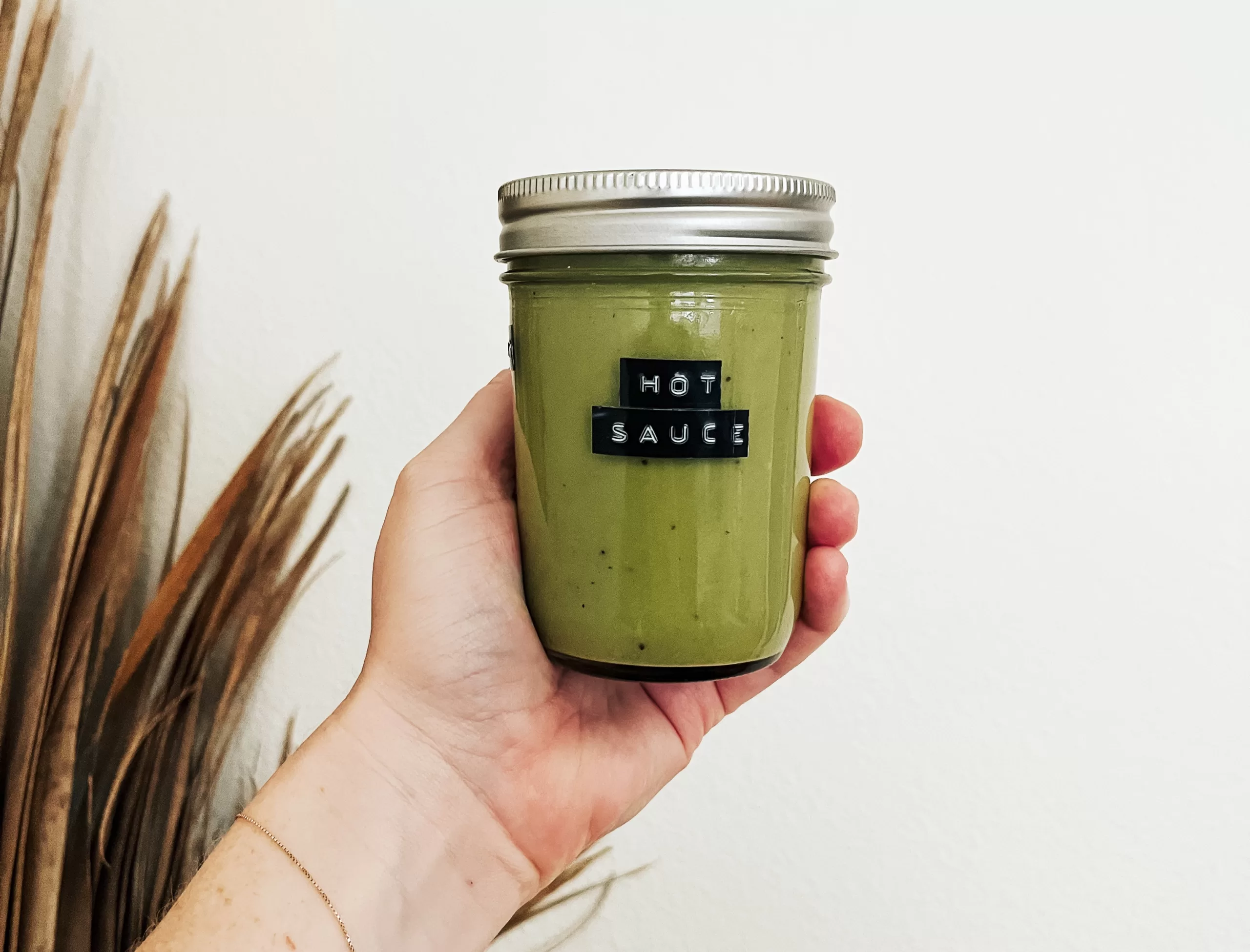 A hand holding a jar of green, homemade hot sauce.