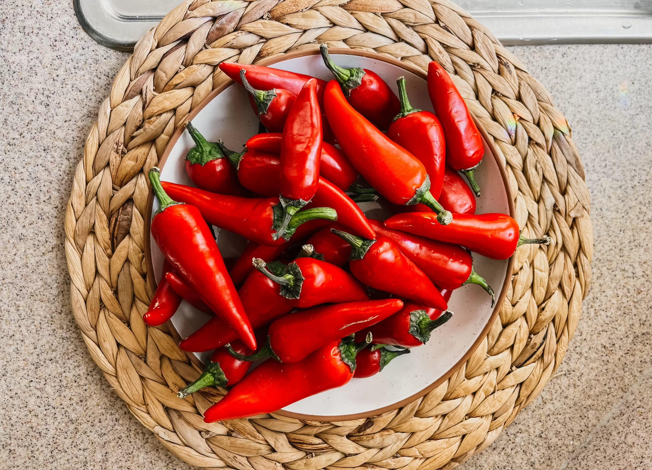 A bowl of red jalapeño peppers on top of a rattan placemat.