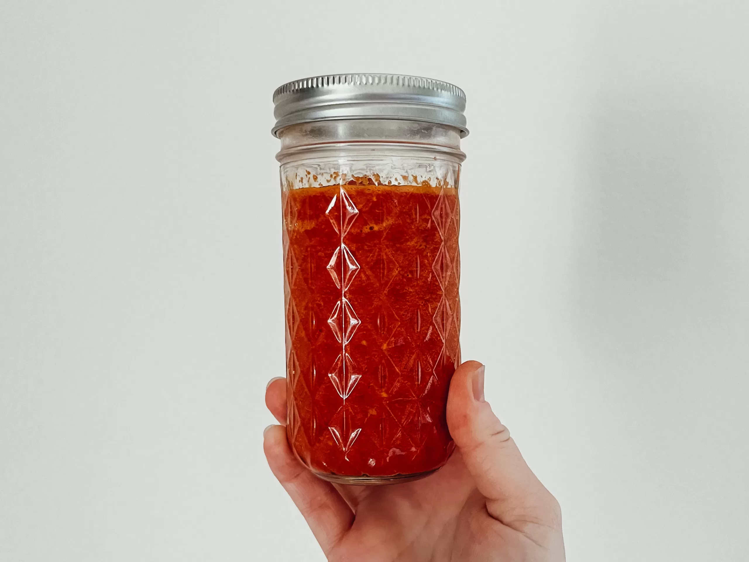 A hand holding a jar of homemade sriracha sauce.