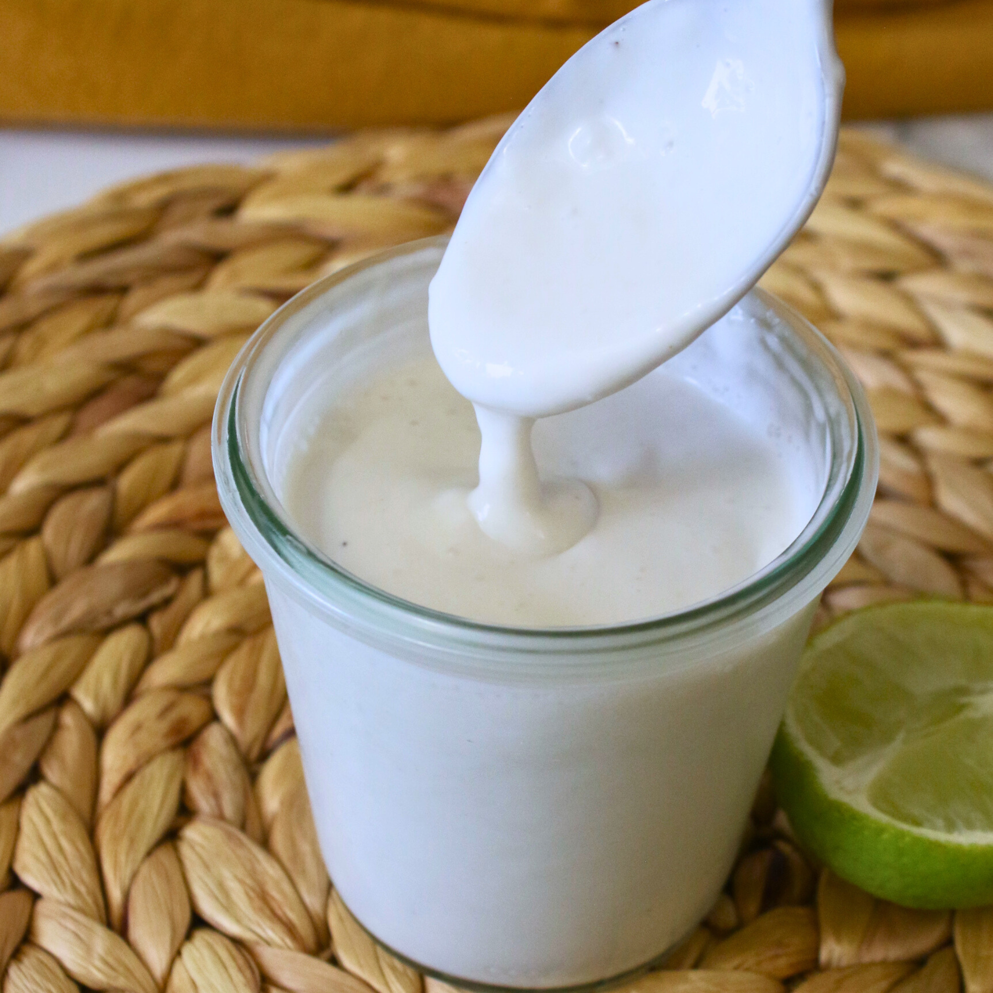 Dairy free sour cream in a glass jar next to a sliced lime.
